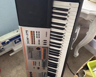 Yamaha PSR-EX5 electronic keyboard with 61 keys, drum pads, and built-in sounds and rhythms. The unit shows normal wear and is displayed in a home setting.