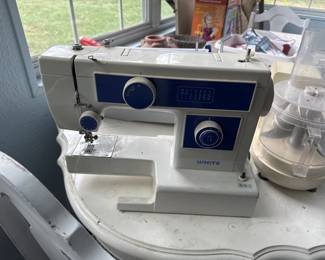 Vintage Elna sewing machine with white and navy blue casing, featuring a dial control panel and built-in light. The machine appears to be in working condition with some surface wear.