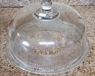 Clear glass dome with ribbed pattern and matching glass base, topped with a knob finial. Used for displaying and protecting cakes or baked goods on a countertop.