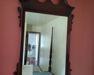 A dark wood framed mirror with decorative carved details along the top and sides. The mirror reflects a doorway and interior hallway.
