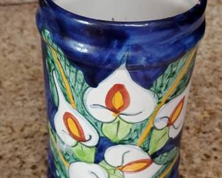 Cylindrical ceramic vase with a deep blue glaze featuring hand-painted white flowers with red and yellow centers and green leaves. The piece appears to be decorative pottery, possibly from a folk art or artisan tradition.