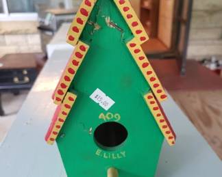 Green painted wooden birdhouse with red and yellow trim and a circular entrance hole. Features simple folk art-style decoration.