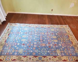 Large hand-knotted or traditional area rug with blue field and floral motifs, featuring a decorative border in warm tones. Shows wear consistent with age and use.