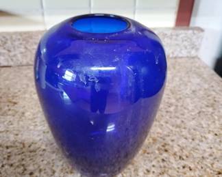 A solid cobalt blue glass vase with a rounded, bulbous body and narrow opening. The piece has a smooth, glossy finish and appears to be hand-blown or molded glass.