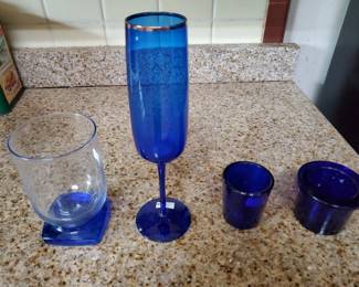 Four-piece set of cobalt blue glass items including a tall flute or champagne glass, a short tumbler, and two additional drinking glasses. All pieces appear to be in good condition.