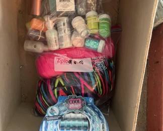 Box containing assorted yarn in various colors, knitting needles, crochet hooks, and other fiber craft supplies. Includes both packaged and loose materials suitable for knitting or crochet projects.