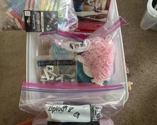 Clear plastic storage container filled with assorted craft supplies including yarn, thread, beads, and various sewing notions. Contents appear to be a mixed collection of crafting materials.