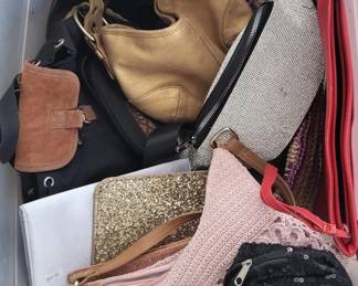 Collection of various handbags and accessories including a tan leather shoulder bag, black hobo-style bag, patterned clutches, and other items in mixed colors and materials.