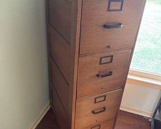 Four-drawer wooden file cabinet with metal handles and label plates. Shows typical wear consistent with office or home use.