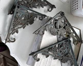 Set of three ornate cast iron shelf brackets with scrollwork and grape vine details. These vintage brackets feature dark patina and can be used to support shelving or as decorative wall accents.