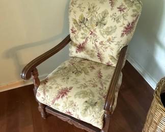 Wooden frame armchair with rolled arms and floral upholstery in cream with burgundy and green botanical pattern. The chair features curved wooden armrests and appears to be in good condition.