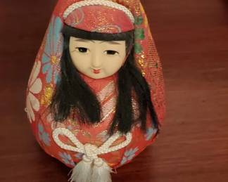 Hand-painted wooden nesting doll with traditional Russian costume featuring a red headscarf and embroidered details. The doll has black hair and a painted face with traditional folk art styling.