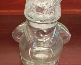 Clear glass decorative bottle shaped like Santa Claus with a removable head stopper. The piece features molded details for facial features and a body form typical of novelty barware or decorative glassware from the mid-20th century.