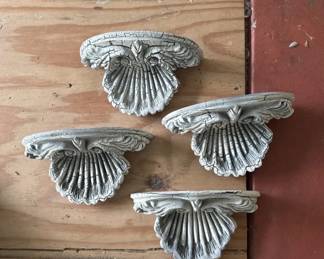 Set of four decorative metal shelf brackets with a scallop shell design and ornamental detailing. Appear to be cast metal, likely brass or similar alloy with a silvery finish.