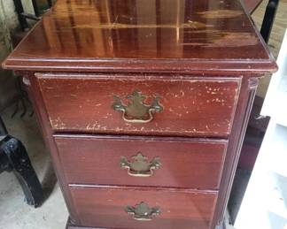 Small wooden nightstand or bedside table with three drawers and brass hardware. Shows wear consistent with age and use.