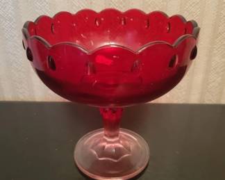 A ruby red glass compote or pedestal bowl with a scalloped rim and footed base. The bowl features a decorative pattern and appears to be vintage glassware.