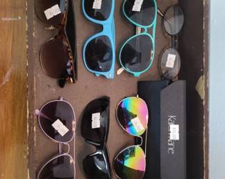 Collection of approximately 8-10 pairs of sunglasses in various styles and colors, including oversized frames, cat-eye shapes, and standard aviator-style frames. Frames appear to be plastic and metal in shades of black, brown, and blue.