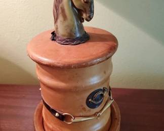 Wooden cylindrical box with a carved horse head finial on the lid and decorative metal band around the middle. The piece appears to be handcrafted with a natural wood finish.