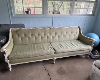 A traditional-style sofa featuring a cream or light beige upholstered seat and back with button tufting, supported by a carved wooden frame with curved arms and legs. The piece shows signs of age and wear consistent with vintage furniture.