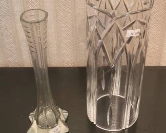 Two clear cut glass vases with geometric patterns. The taller vase on the right features a diamond and line design, while the smaller bud vase on the left has vertical cuts and decorative handles.