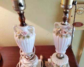 Two matching table lamps with cream-colored ceramic urn-shaped bases featuring floral relief details and brass hardware. Each lamp is topped with what appears to be a brass socket and finial.