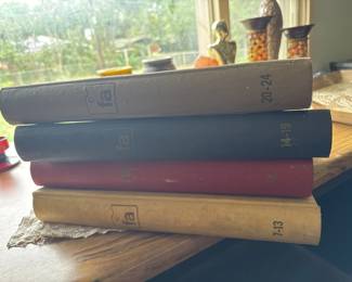 Four hardcover books in various colors stacked together, appearing to be from mid-20th century based on their cloth binding and spine design. Condition shows typical wear consistent with age.