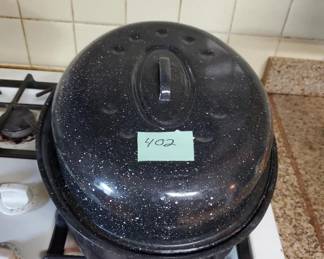 Black speckled enamel canning or cooking pot with matching domed lid and metal handles. Shows age and wear with surface marks and discoloration.