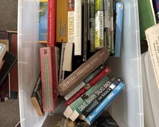 Assorted collection of books and DVDs stored in a clear plastic bin, including various titles in different genres and formats.