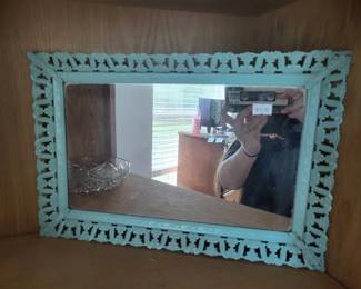 Rectangular wall mirror with a turquoise-painted wooden frame featuring decorative carved or stamped detailing around the border. The mirror appears to be in good condition with visible reflections.