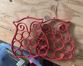 Pair of red plastic owl-shaped hangers with multiple circular loops designed to hold scarves, belts, or similar accessories. Each hanger features decorative spiral details and hangs from a hook.