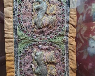 A length of ornamental trim featuring embroidered dragons or mythical creatures in metallic threads on a burgundy and green background. The piece appears to be vintage or antique with detailed needlework and metallic accents.