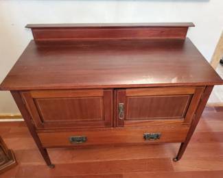 Early 20th century wooden sideboard with two cabinet doors, two drawers, and tapered legs. The piece features a warm reddish-brown finish and simple hardware.