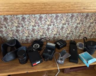 Assorted camera lenses and photography equipment including what appears to be telephoto and standard lenses with various black lens caps and cases. Includes at least one lens box visible on the right side.