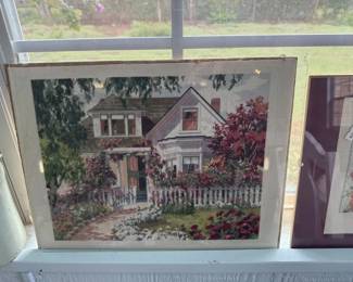 Framed print depicting a charming two-story house with white picket fence and flowering vines. The artwork appears to be a watercolor or similar medium in a simple frame.