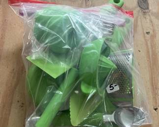 A collection of green-handled kitchen tools including graters, peelers, and other vegetable preparation implements, still in original packaging.