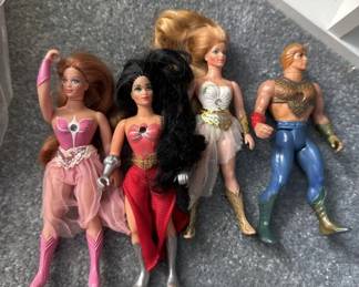 Lot of four vintage Barbie and Ken dolls in various outfits, including a blonde Barbie in pink, a brunette in red, a blonde in white, and a Ken doll in blue pants. Dolls show age-appropriate wear and are sold as pictured.