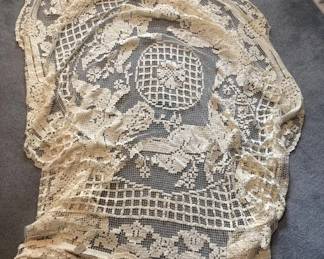 Delicate cream-colored lace collar or decorative appliqué featuring intricate floral and geometric patterns. The piece shows age and wear consistent with vintage textiles.