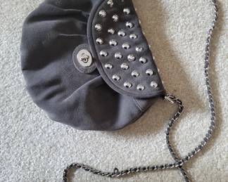 Small black fabric clutch with silver stud detailing and a silver-tone chain strap. Features a snap closure and is suitable for evening wear or special occasions.