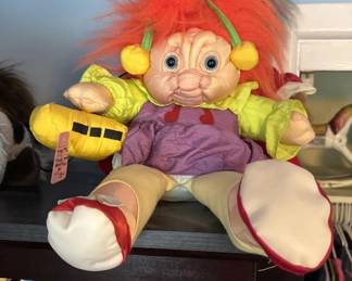 A vintage troll doll with bright red hair, yellow limbs, and purple clothing. The doll features the characteristic large eyes and exaggerated features typical of 1980s-90s troll dolls.