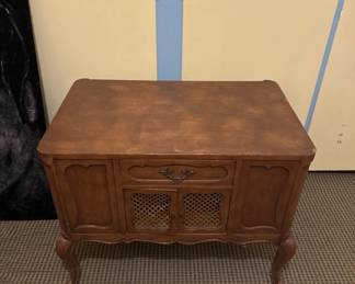 Mid-century wooden console cabinet with a single drawer and two lower cabinet doors featuring rattan or woven panels. The piece sits on curved legs and shows a warm wood finish.