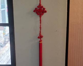 A handmade red macramé wall hanging with knotted diamond shapes and a tassel at the bottom. Typical of 1970s-80s home décor.