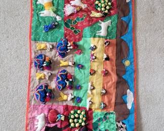 A decorative fabric panel featuring vibrant rainbow-colored sections adorned with various beads, sequins, and embellishments. The piece appears to be handmade or artisanal, with a pink binding along the edges.