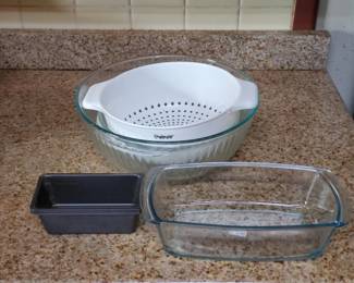 Three-piece kitchen collection including a white plastic colander with handles, a black rectangular baking dish, and a clear glass rectangular baking pan.