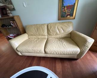 Two-seat loveseat upholstered in cream-colored leather with padded armrests and cushioned seating. Shows normal wear consistent with use.