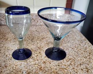 Two drinking glasses with cobalt blue rims and bases—one appears to be a water or wine glass, the other a wider margarita or cocktail style. Both are clear glass with matching blue trim.