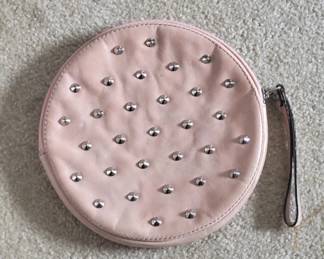 Small round cosmetic or jewelry pouch in pale pink quilted fabric with silver stud detailing and a wrist strap. Practical for travel or everyday use.