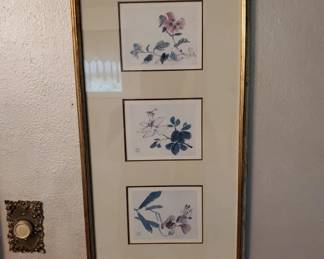 Three small framed botanical prints arranged vertically in a single frame with gold-tone border and tan matting. Each print features delicate watercolor-style flowers and foliage in blue and purple tones.