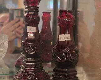 Pair of deep ruby red glass decanters with decorative stoppers and embossed floral or geometric detailing on the bodies. Both pieces show the characteristic rich color and ornamental style typical of vintage glassware.