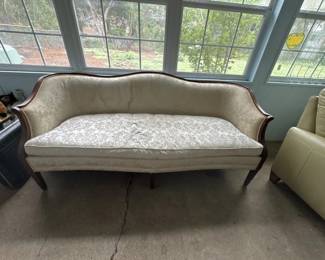 A traditional settee with curved wooden frame and neutral upholstery, featuring a cushioned seat and back. The piece shows some wear and discoloration consistent with age and use.