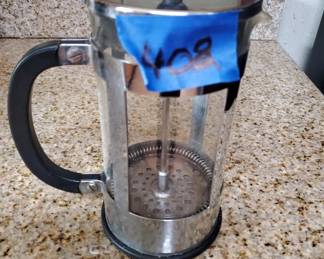 Glass carafe with black handle and blue lid, appears to be a pour-over or drip coffee maker component. Shows some wear and has a handwritten mark on the lid.